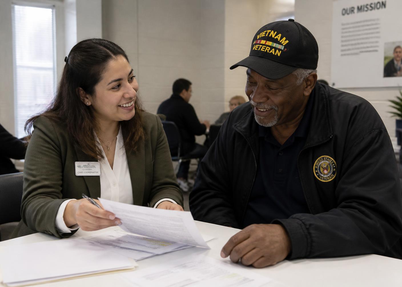 A MissionCare housing coordinator reviewing documents with a veteran at a community center table